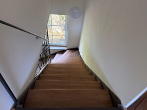 Uma escadaria de madeira com corrimão de metal, que leva a um quarto com janela.