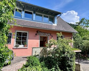 A building with a sign reading 'DorfCafe' and a window with a view of the interior.