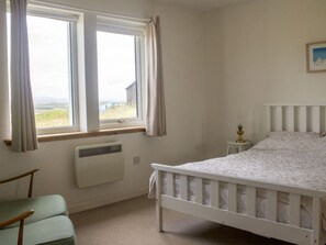 Ein Schlafzimmer mit Bett, Stuhl, Heizkörper, einem Fenster mit Vorhängen und einem Bild an der Wand.