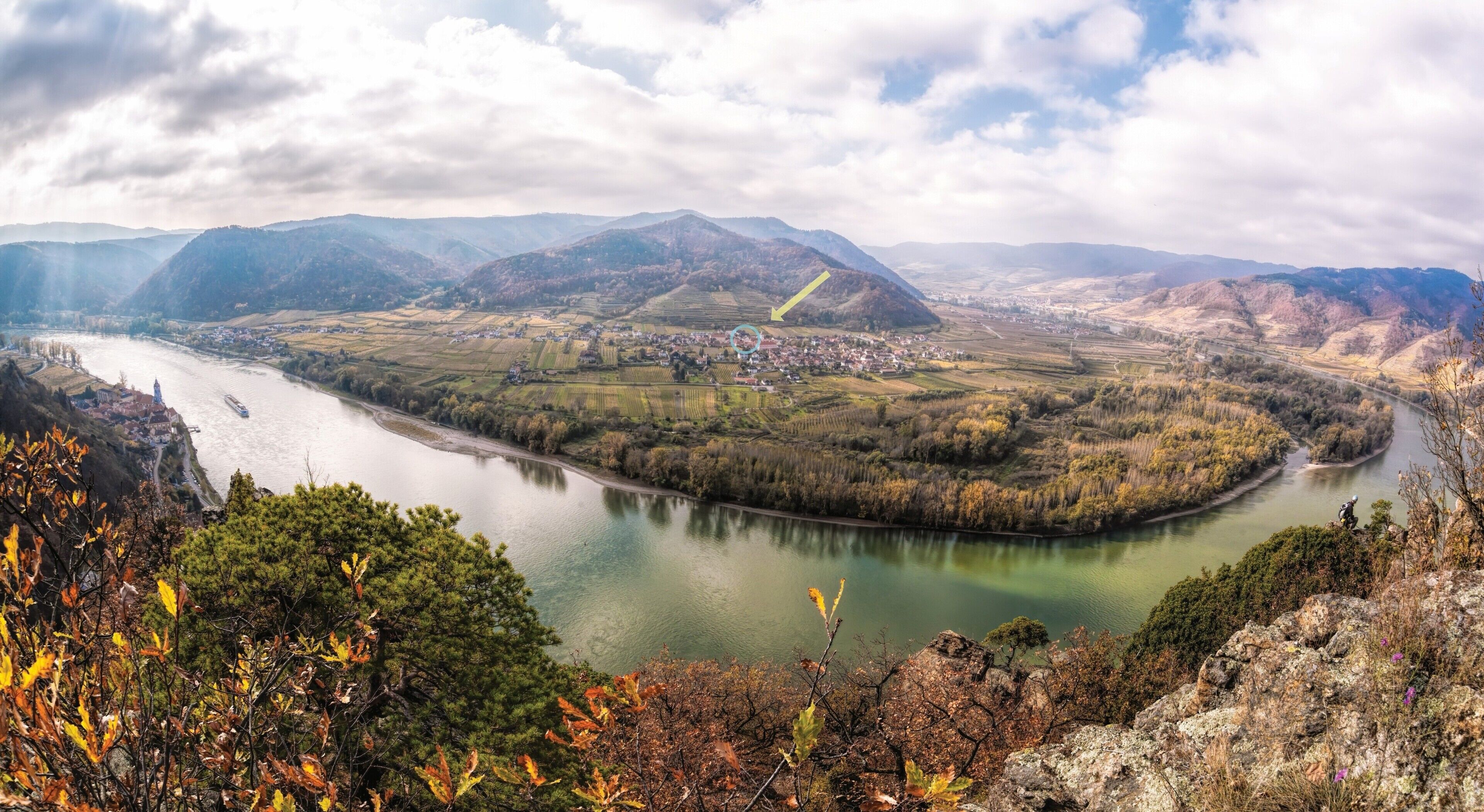 Um rio serpenteia por um vale, com uma cidade na margem e montanhas ao fundo.