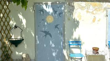 A door with a bird mural, a wall-mounted sink, a blue chair, and a small table with a potted plant.