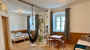 Ett rum med en säng, en hängstol, ett bord med stolar, en bokhylla och ett fönster med gardiner.