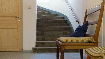 A staircase with a wooden handrail, a wooden chair with a cushion, and a brown rug on the floor.