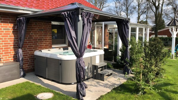 A hot tub with a covered patio area, a brick wall, and a small garden.