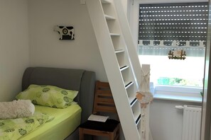 A bedroom with a bed, a chair, a desk, a ladder, a radiator, and a window with blinds. - Holiday Home with Hot Tub and Sauna near Bernsteinsee (Wiefelstede)
