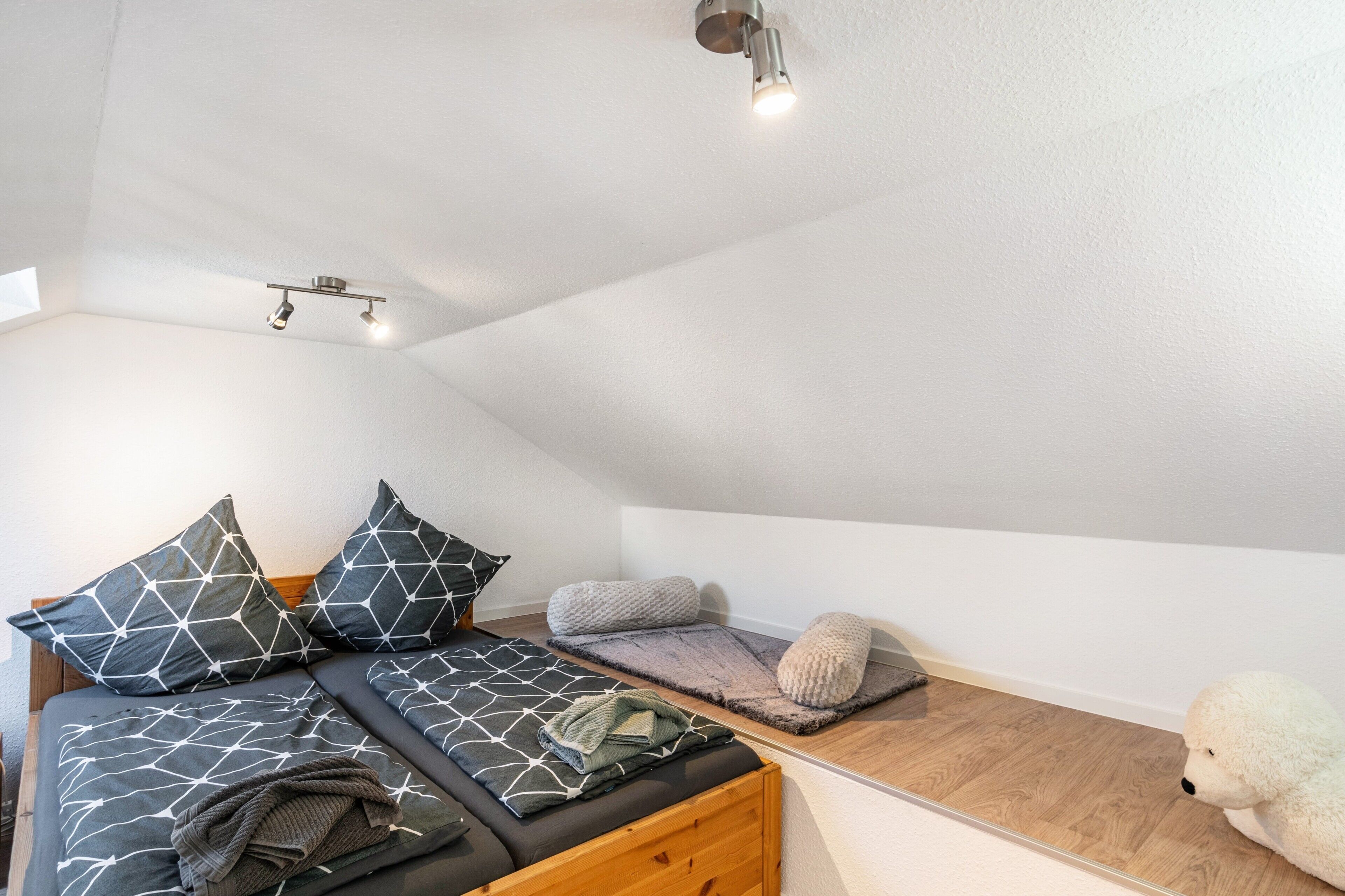 Een moderne loft slaapkamer met schuine plafond, een bed met beddengoed met geometrische patronen, een pluizige witte hond en een dakraam.