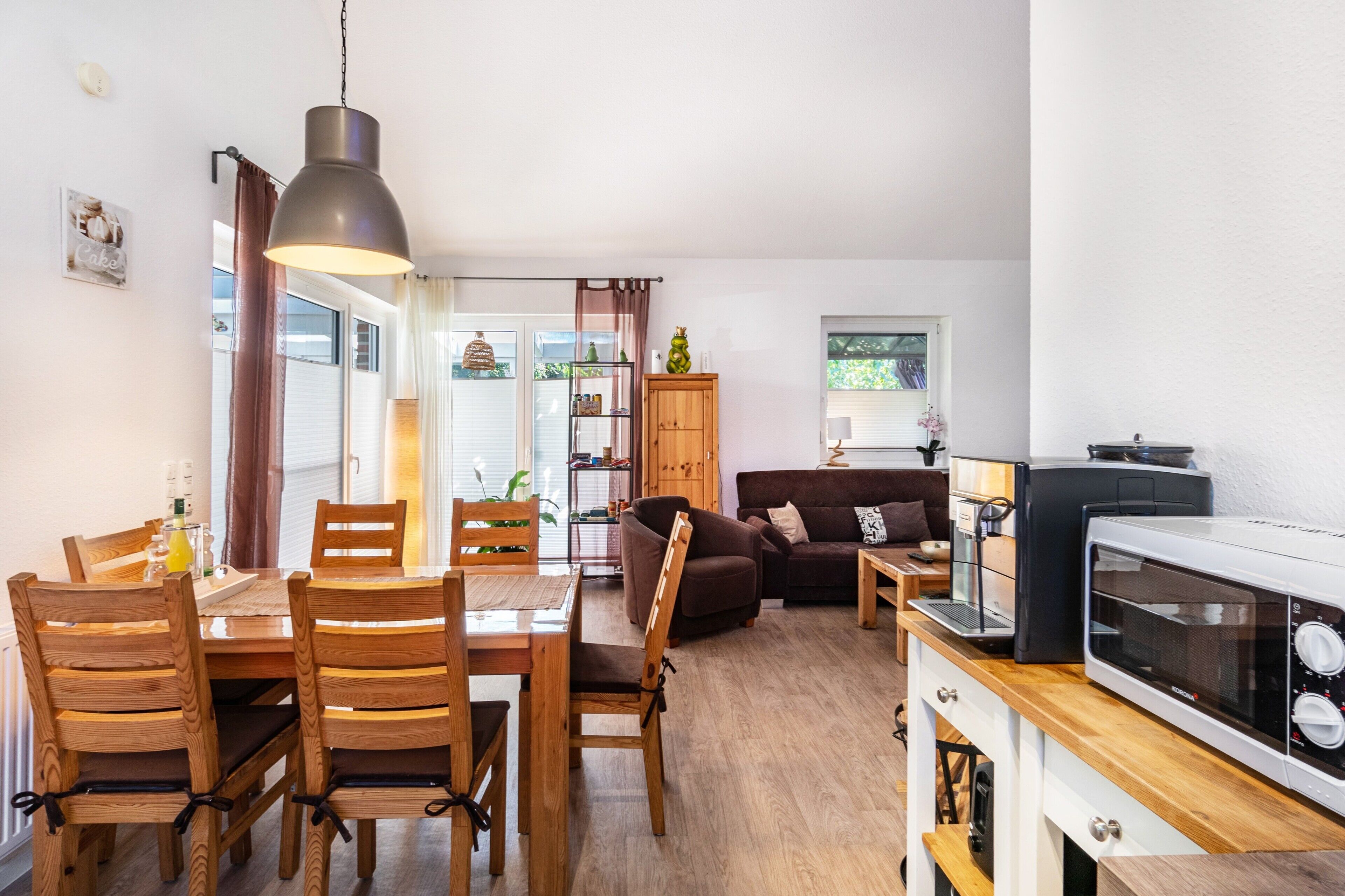 Een knus woongedeelte met een eethoek, een bank, een kitchenette en een houten eettafel met stoelen.