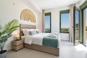 A bedroom with a bed, bedside table, lamp, and a view of the sea. - Villa Meraki - Sea View (Chania)