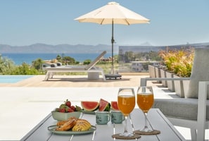 A table with food and drinks, a beach view, and a mountain in the background. - Villa Meraki - Sea View (Chania)