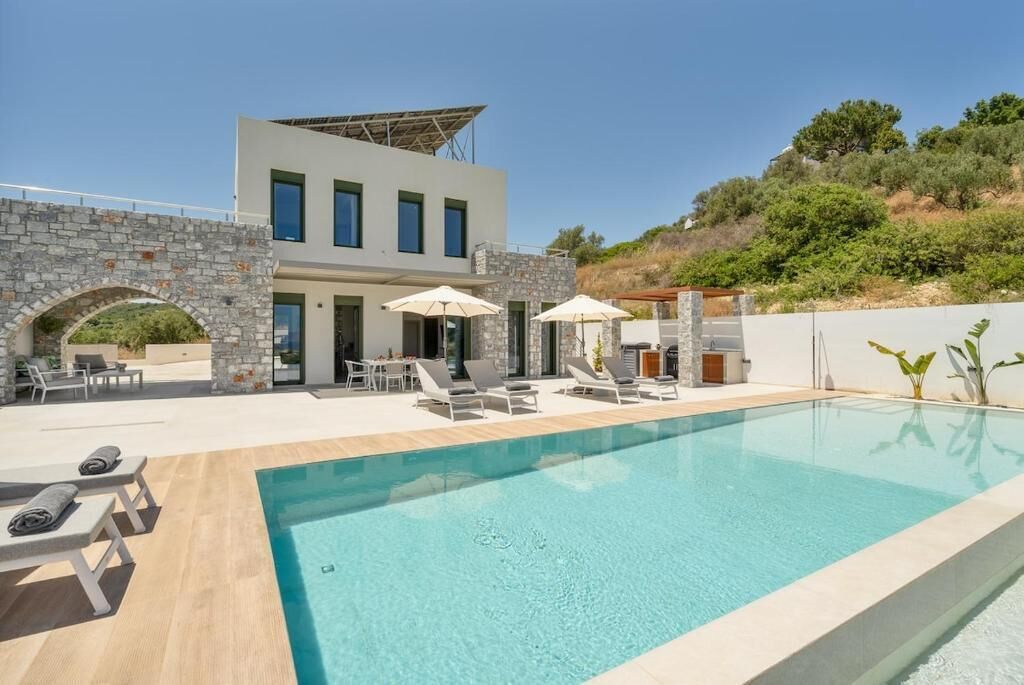 A modern building with a swimming pool, outdoor seating, and stone arches.