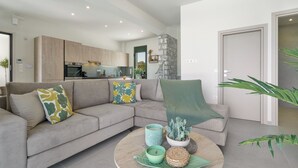 Un salon moderne avec un canapé gris, une table basse ronde et une cuisine en arrière-plan.