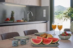 A modern kitchen with a view of the outdoors, featuring a dining table set with food and drinks. - Villa Meraki - Sea View (Chania)