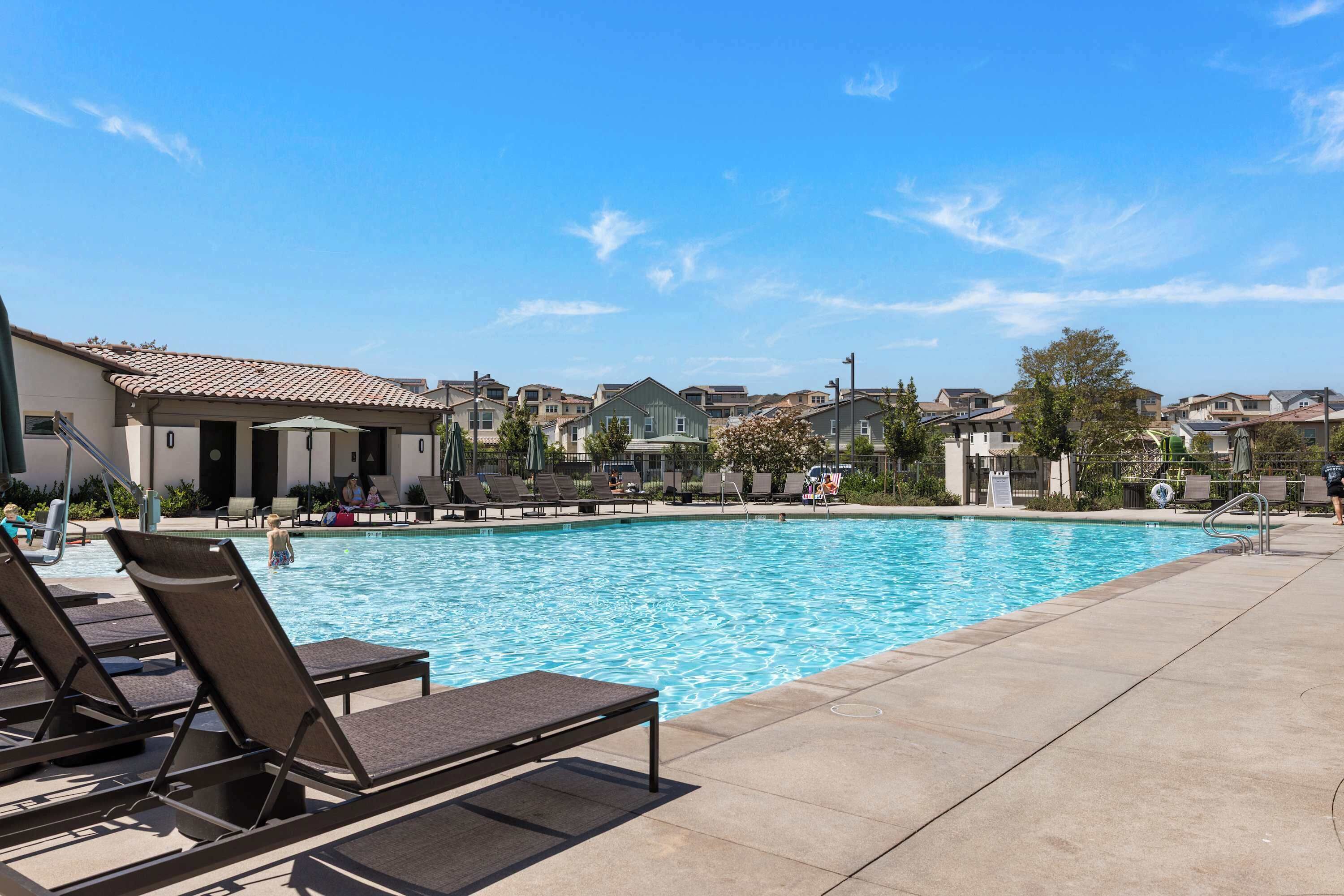 Una piscina con sillones de descanso, cielo despejado y edificios residenciales al fondo.