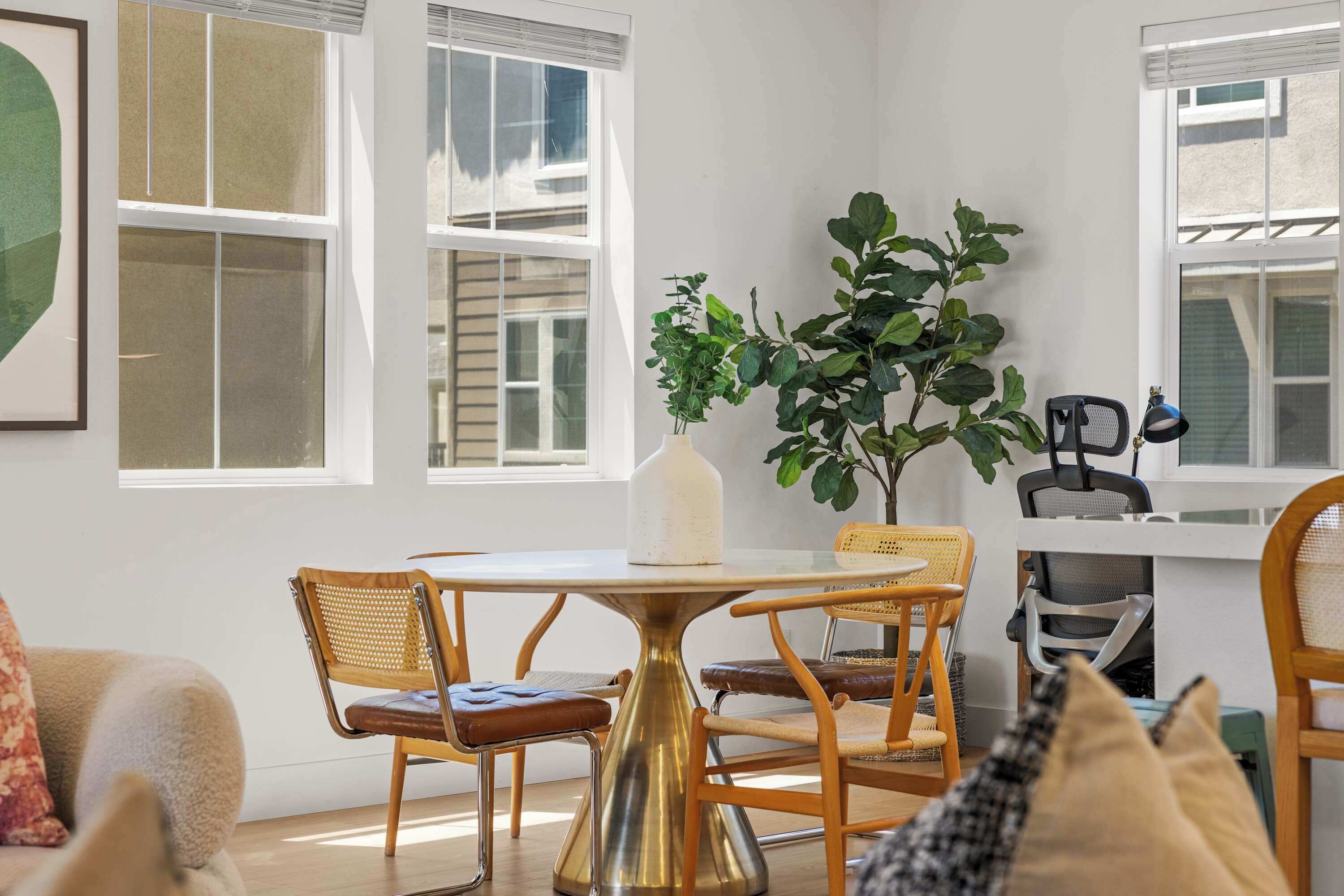 A room with a round table, chairs, a potted plant, and a window with blinds.
