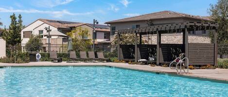 Una piscina con sillones de descanso y una pérgola, rodeada de edificios residenciales.