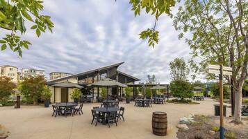 An outdoor patio area with multiple tables and chairs, a covered seating area, and a building with a sloped roof.