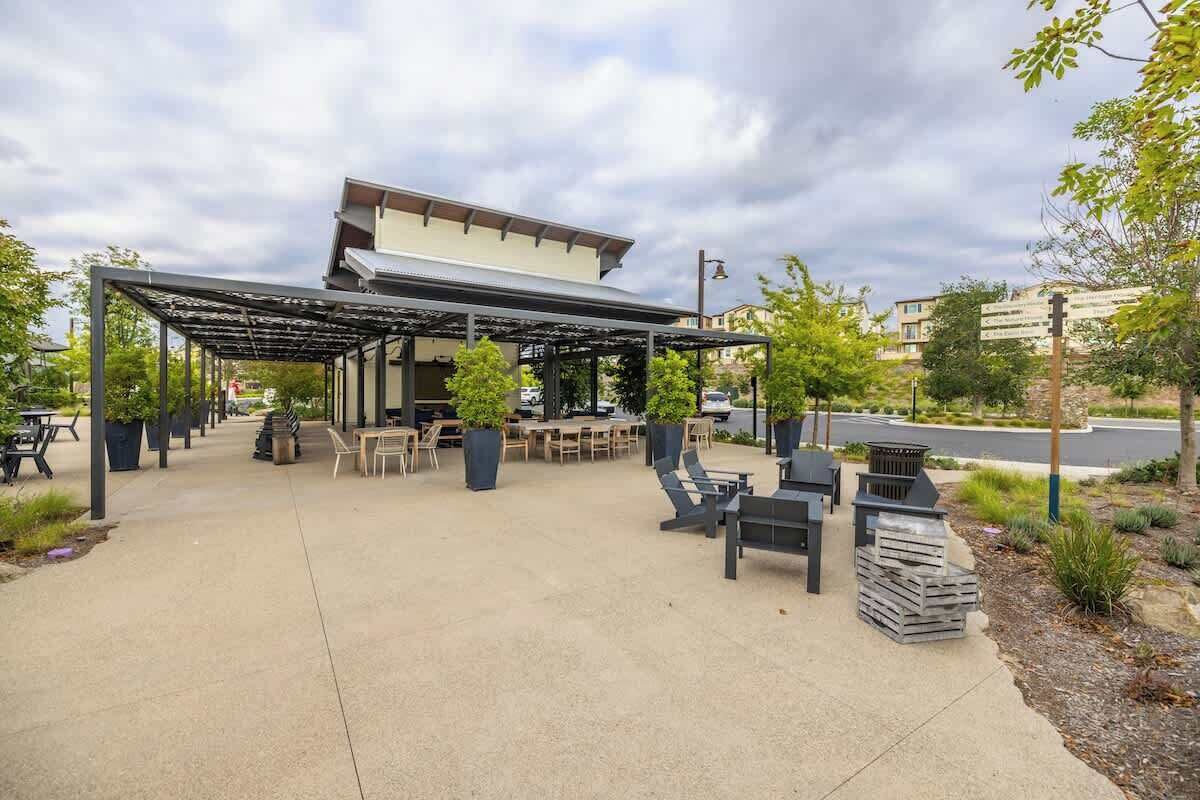An outdoor patio area with tables and chairs, a covered seating area, and a building in the background.