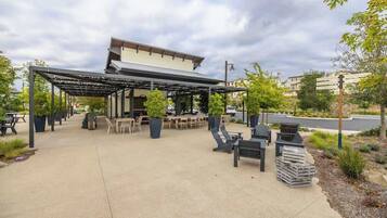 An outdoor patio area with tables and chairs, a covered seating area, and a building in the background.