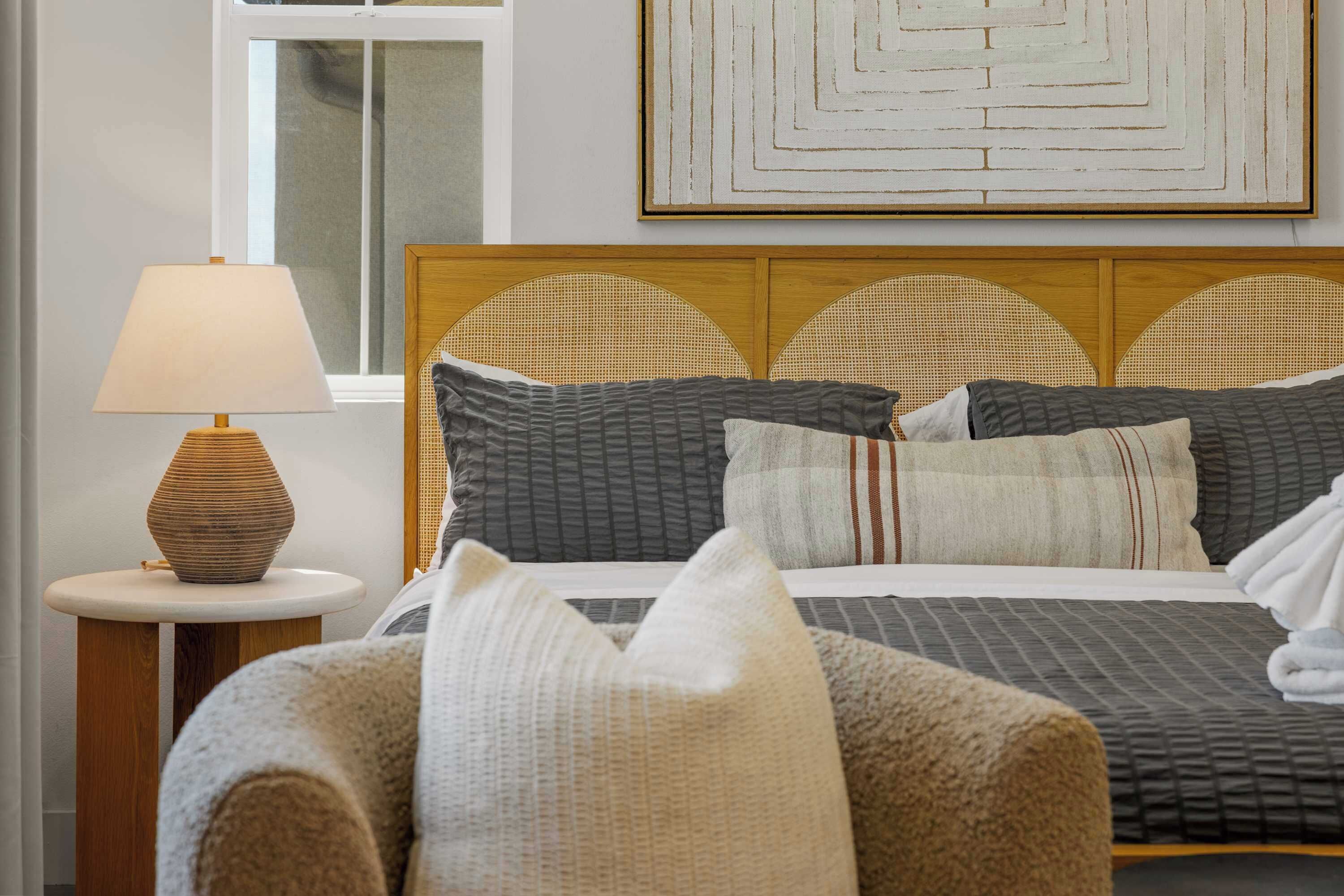 A neatly arranged hotel room with a bed, pillows, a lamp, and a wall art piece.