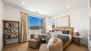 A bedroom with a bed, two armchairs, a bookshelf, a window with a view, and a painting on the wall. - @ Marbella Lane - Designer Dream Oasis Family Home (San Juan Capistrano)