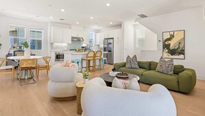 A modern living space with a dining area, kitchen, and a green sofa with decorative pillows. - @ Marbella Lane - Designer Dream Oasis Family Home (San Juan Capistrano)