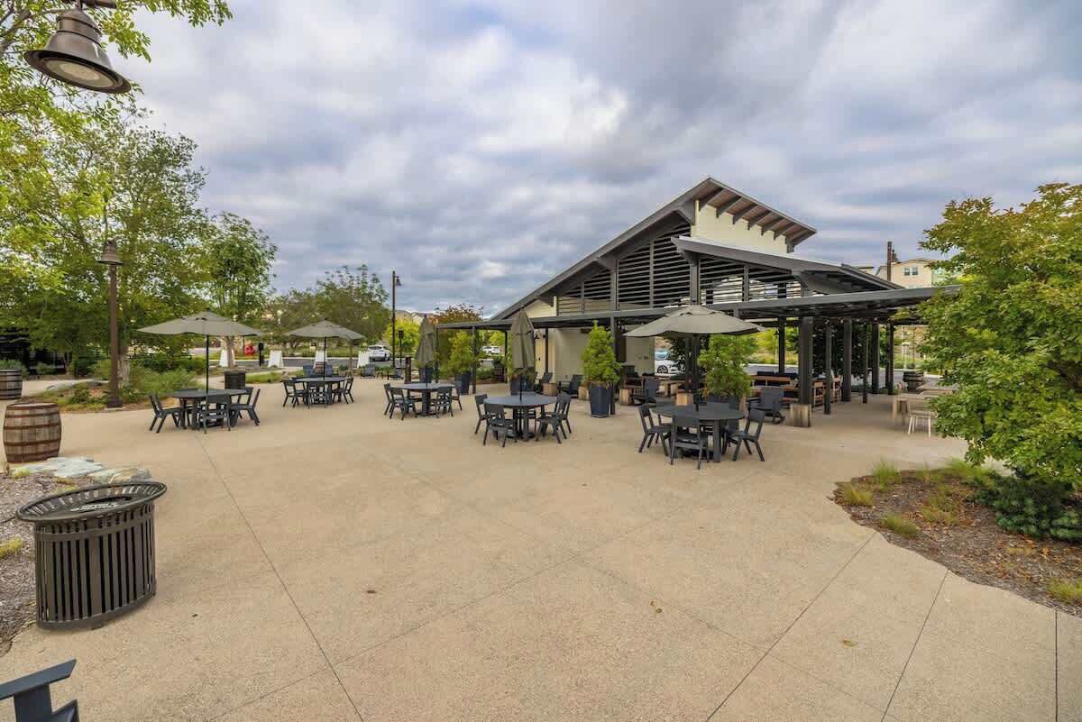 An outdoor patio area with tables and chairs, a covered seating area, and a building with a sloped roof.