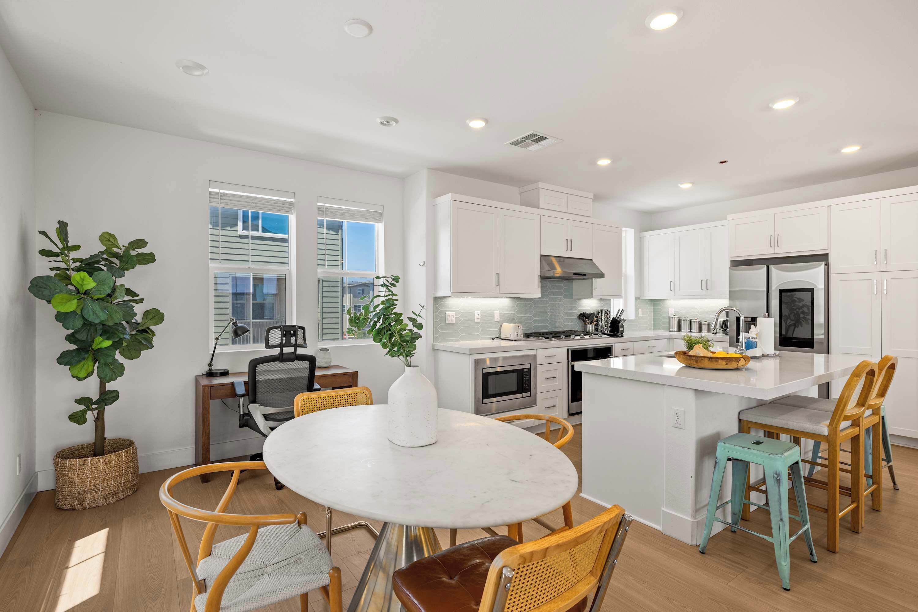 A modern kitchen with white cabinets, a central island, and a dining area with wicker chairs.