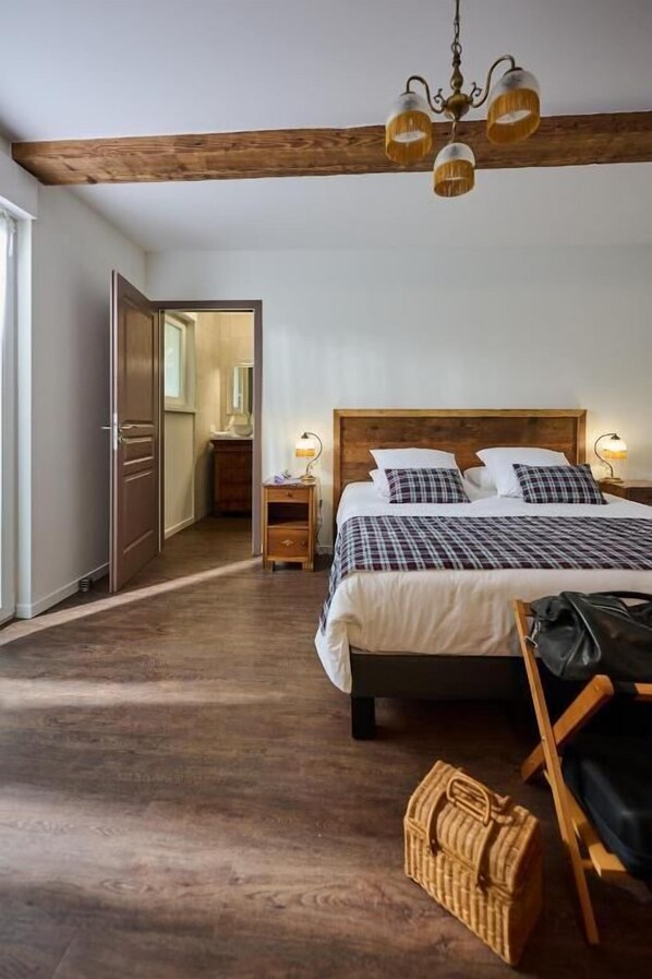 A bedroom with a wooden bed, a chandelier, a nightstand, and a wicker basket. - Le Clos de la Vieille Dame (Sessenheim)