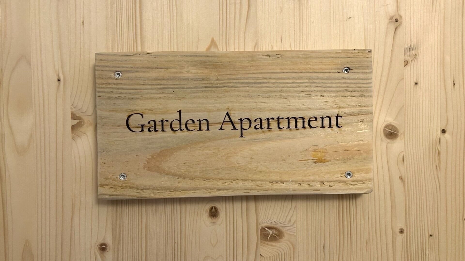 A wooden sign with the text 'Garden Apartment' mounted on a wooden wall.