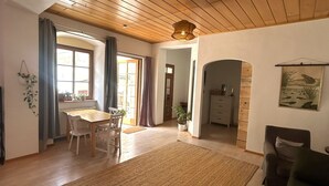 A dining area with a wooden table and chairs, a rug, and a view through an archway to another room. - Danube Atelier – The Garden Apartment (Rossatz-Arnsdorf)