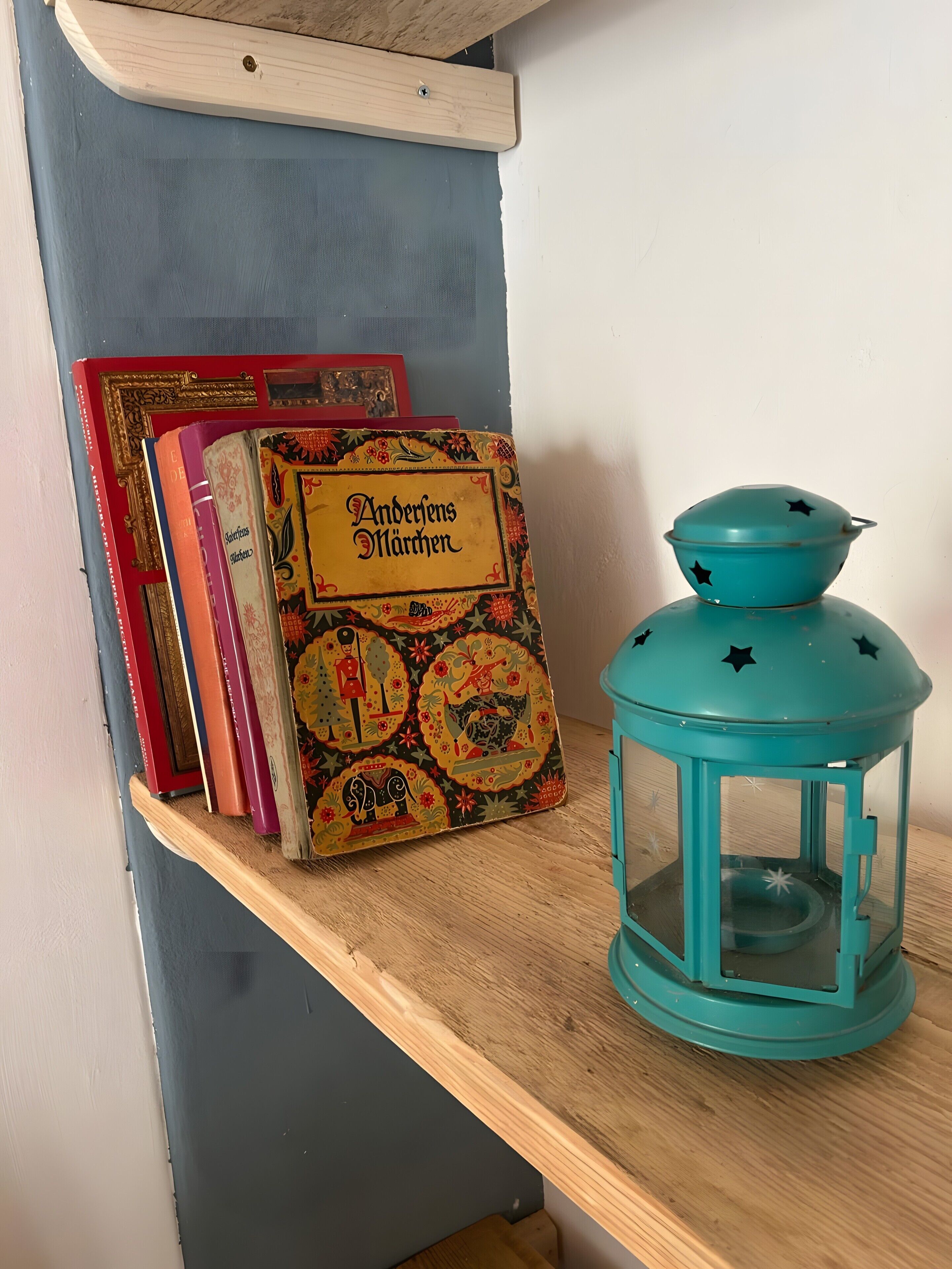 A shelf with books and a teal lantern.