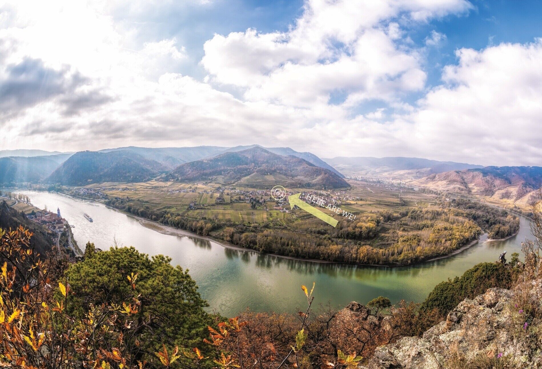 Un valle fluvial con un pueblo, montañas y follaje otoñal.
