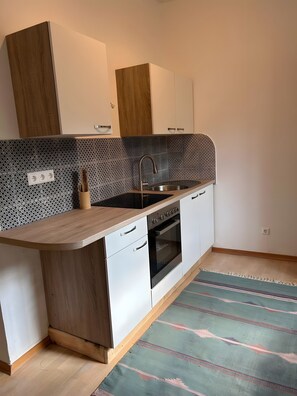 A modern kitchen with a wooden countertop, built-in oven, and white cabinetry. - Danube Atelier – The Garden Apartment (Rossatz-Arnsdorf)