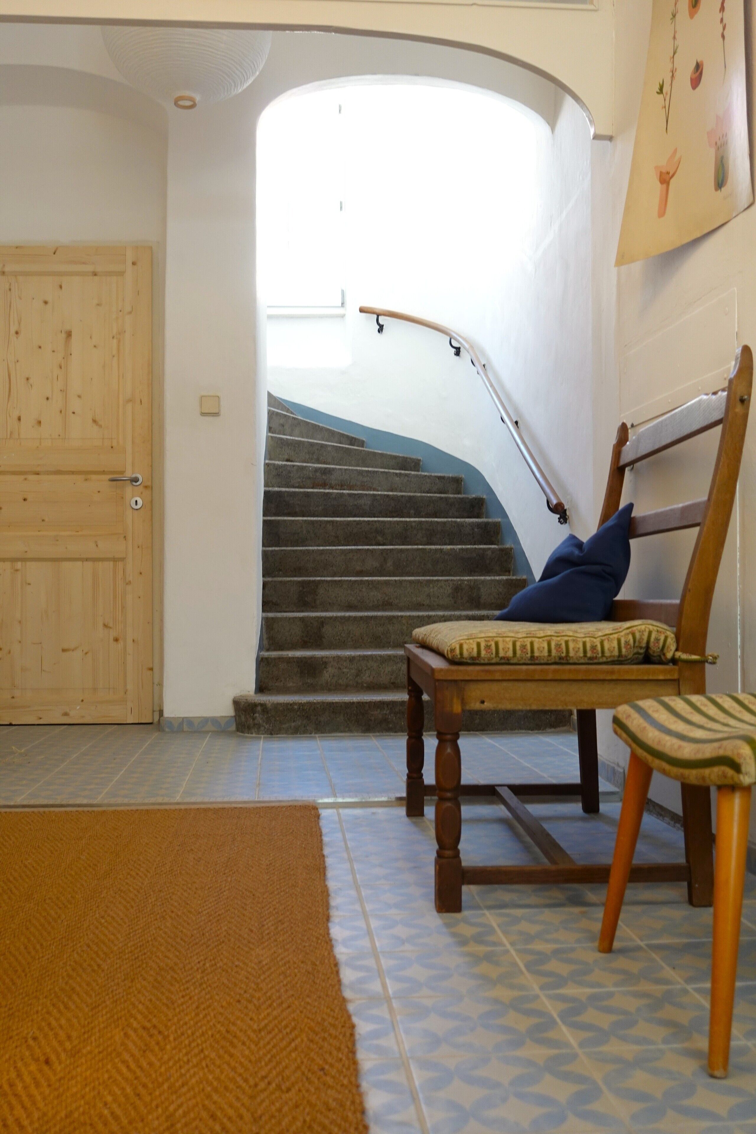 Un escalier avec une rampe en bois, une chaise en bois avec un coussin et un tapis marron sur le sol.