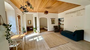 A spacious living area with a wooden ceiling, a dining table with chairs, a sofa, and various plants. - Danube Atelier – The Garden Apartment (Rossatz-Arnsdorf)