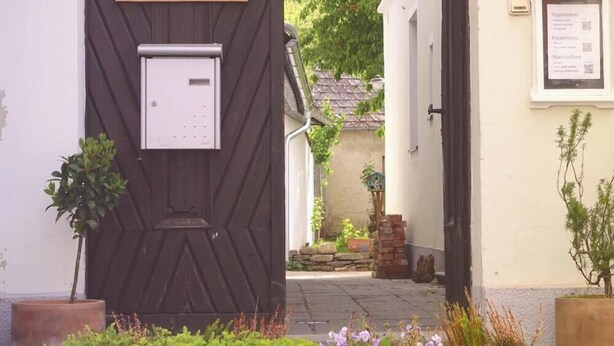 Um edifício com porta de madeira identificada com a palavra 'Yoga', uma placa indicando 'Volksschule' e um quadro de avisos com informações.