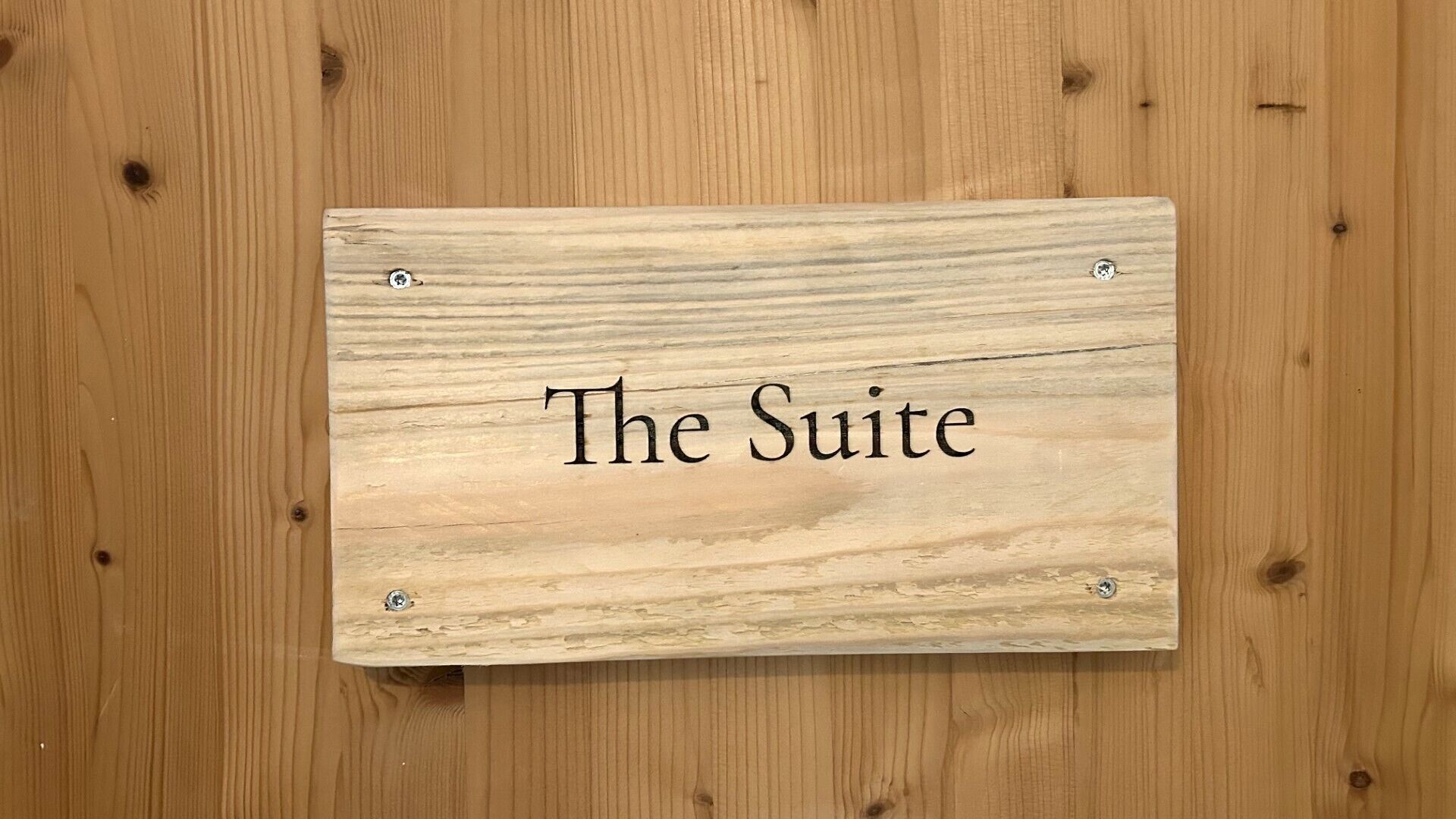 A wooden sign with the text 'The Suite' mounted on a wooden wall.