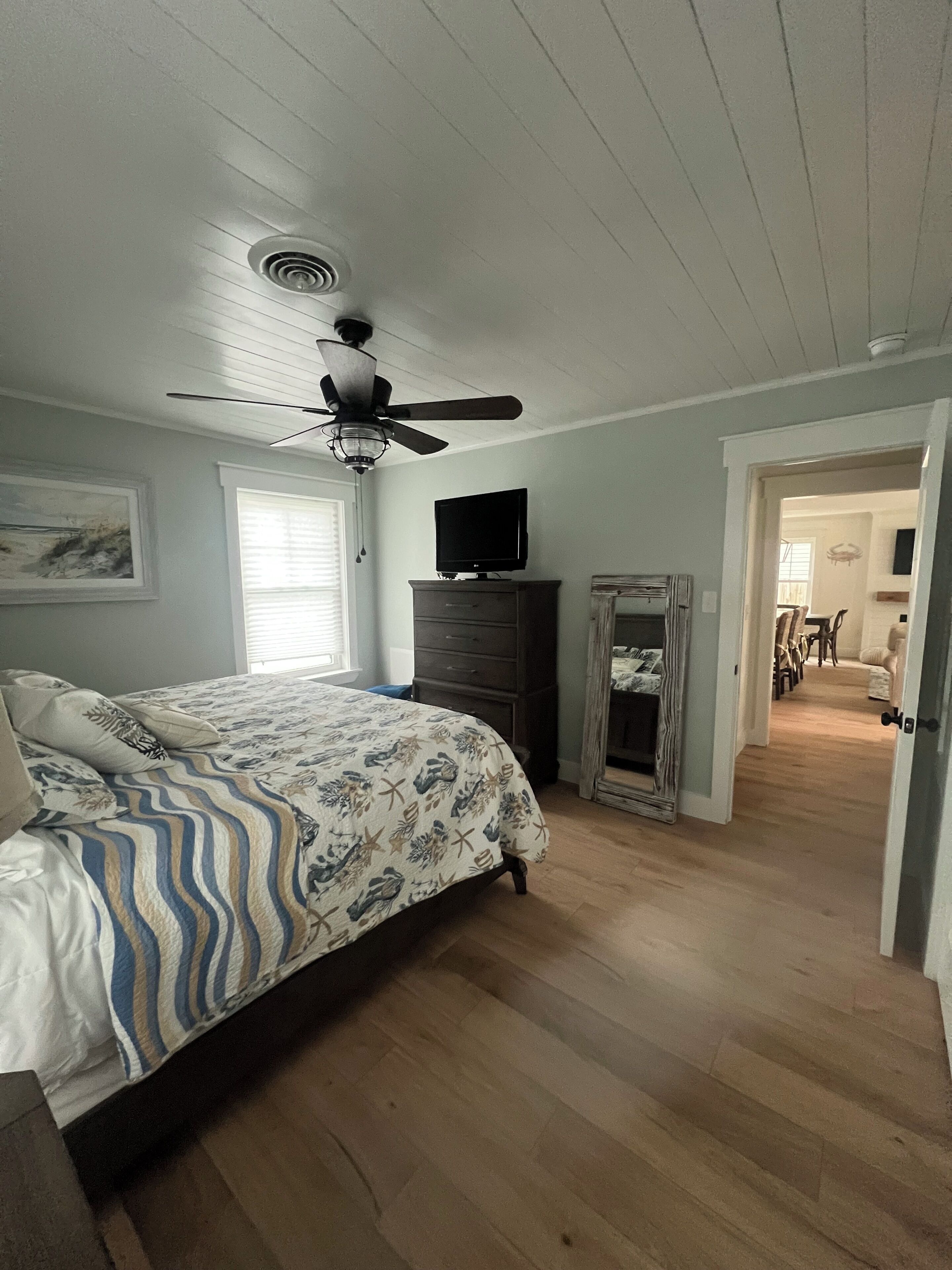 Un dormitorio con cama, ventilador de techo, cómoda, televisor y espejo.