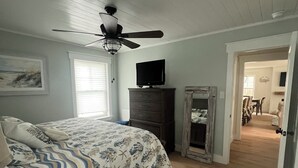 Een slaapkamer met een bed, een plafondventilator, een dressoir, een televisie en een spiegel.
