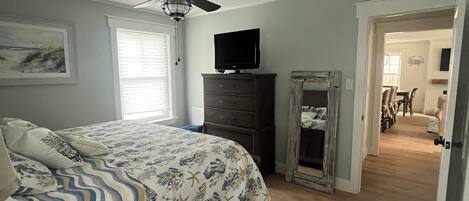 Un dormitorio con cama, ventilador de techo, cómoda, televisor y espejo.
