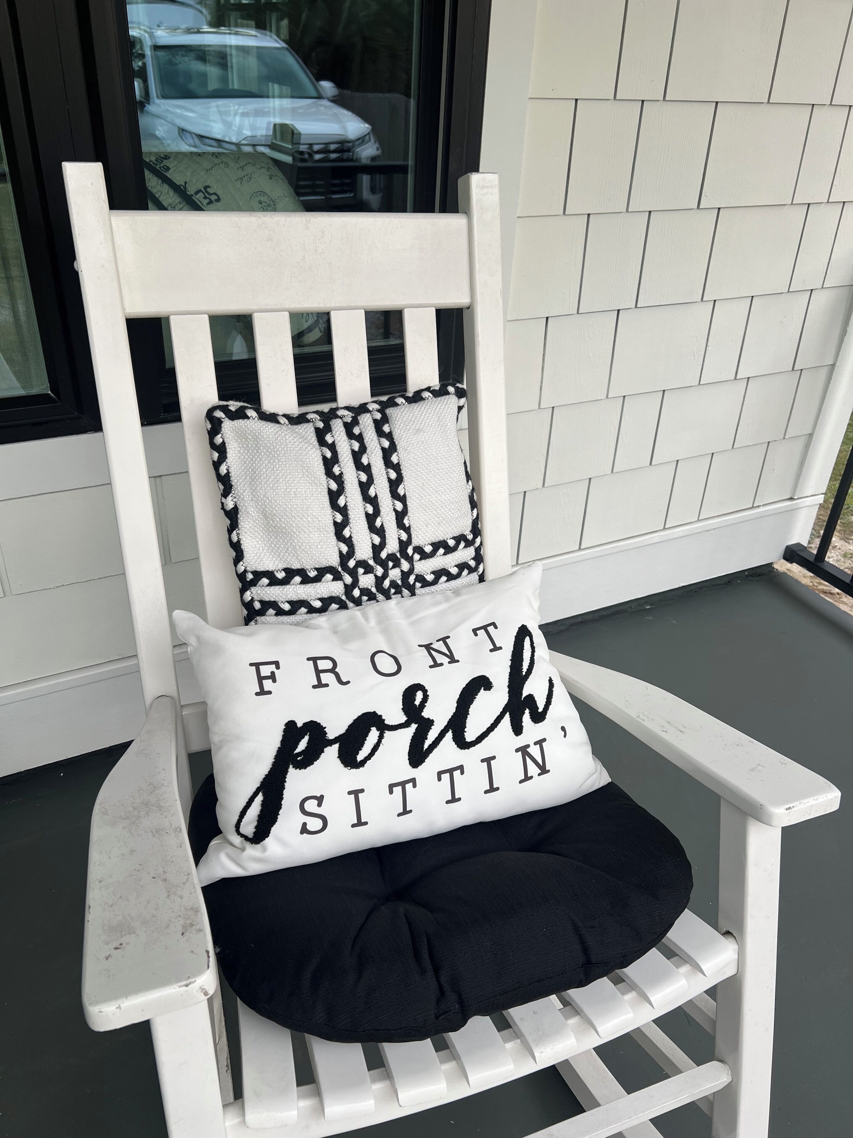 A white wooden chair with a cushion that reads 'FRONT porch SITTIN'.'