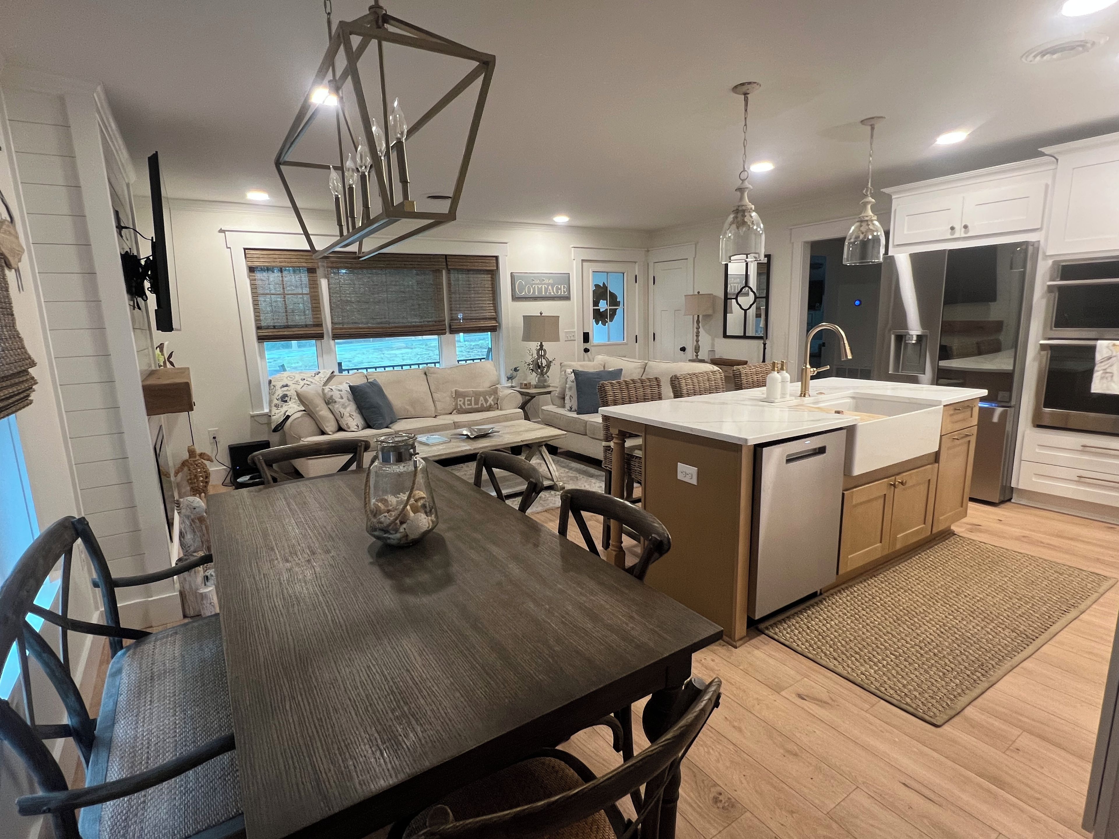 A modern kitchen with a central island, dining area with a table and chairs, and a living area with a sofa and cushions.