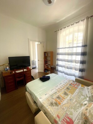 A bedroom with a bed, a desk with a television, a bookshelf, and a window with curtains. - Apartment in the center of Nice (Nice)