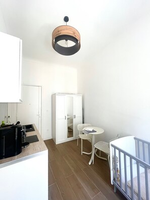 A compact room with a kitchenette, a dining area with a table and chairs, a crib, and a wardrobe. - Apartment in the center of Nice (Nice)
