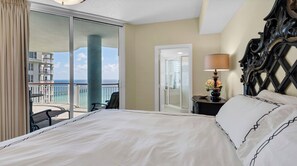 A hotel room with a bed, a chair, a nightstand with a lamp, and a view of the ocean. - Navarre Beach Colony Gulf Front  / West 15B w/chair service (Navarre)