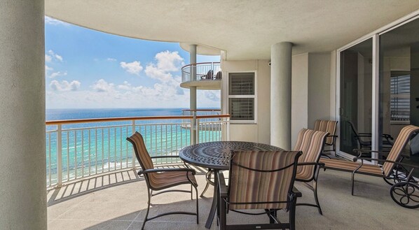A balcony with a round table and chairs, a glass door leading to an interior space, and a view of the ocean. - Navarre Beach Colony Gulf Front  / West 15B w/chair service (Navarre)