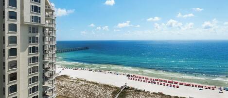 A beachfront hotel with a view of the ocean, a pier, and beach umbrellas.