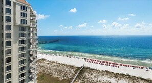 A beachfront hotel with a view of the ocean, a pier, and beach umbrellas. - Navarre Beach Colony Gulf Front / West 15B w/chair service (Navarre)