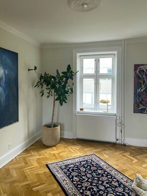Ein Zimmer mit großem Fenster, einem Blumentopf, einem gemusterten Teppich und einem Bild an der Wand.