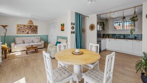Un salon moderne comprenant un canapé, une table à manger et des chaises. On y trouve également un coin cuisine avec des placards et une fenêtre.